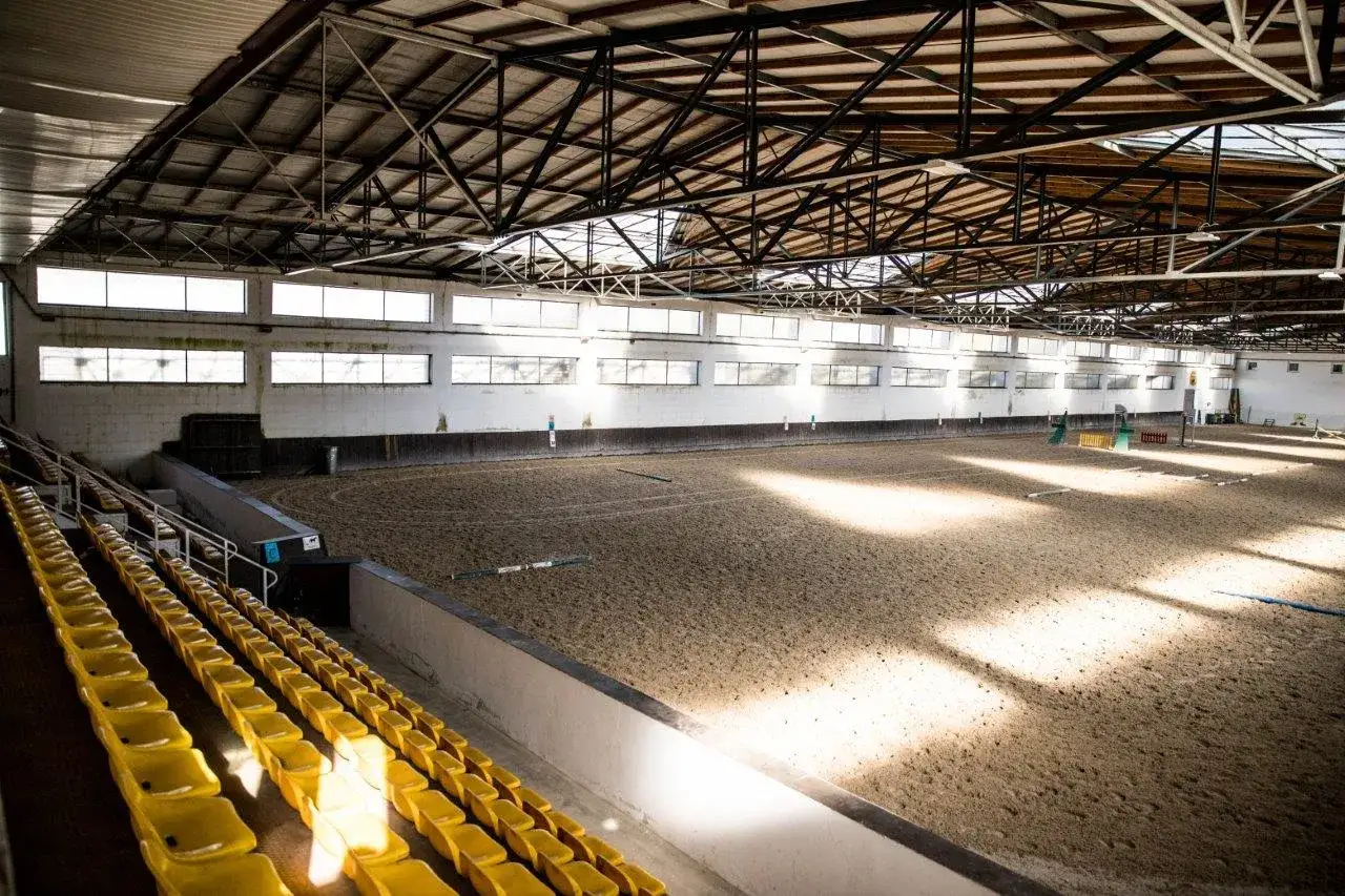 Wnętrze ujeżdżalni w klubie jeździeckim Aromer Stołeczna Józefin. Pusta arena z piaskiem i żółte trybuny czekają na jeźdźców.