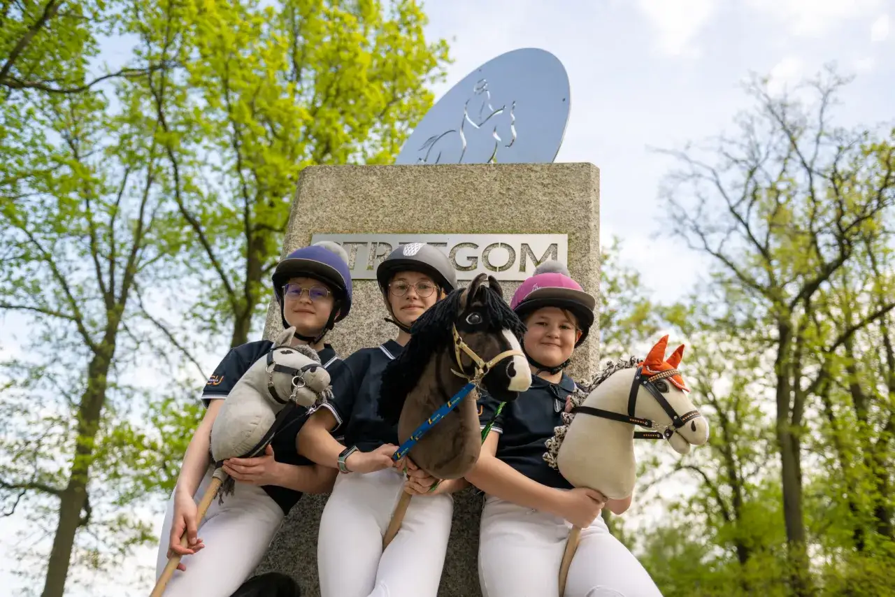 Trzy dziewczynki w kaskach trzymają swoje hobby horse. To popularne hobby, gdzie na patyku zamocowana jest głowa konia.